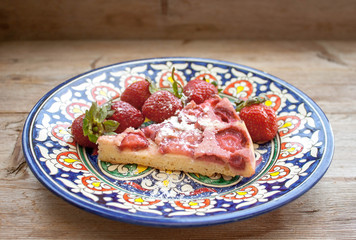 Piece of round strawberry berries tart pie pudding on plate with blue pattern on rustic wooden background