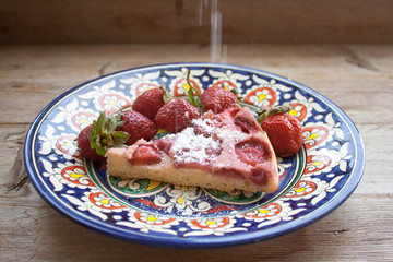 Piece of round strawberry berries tart pie pudding on plate with blue pattern on rustic wooden background