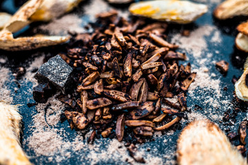 Popular Indian and Asian mukhwas or mouth freshener i.e. Aam Ki Ghuthli Ka Mukhwas consisting of ghee and hard-boiled mango seeds in a bowl on a wooden surface.Along with some raw dried mango seeds.