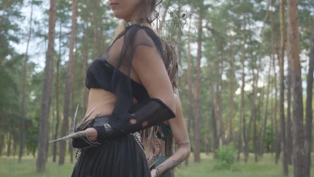 Confident women dancers with make-up and in mystical fabulous costumes dancing groovy dance in nature. Forest fairies, dryads have fun among the trees. Performance of dancers outdoors.