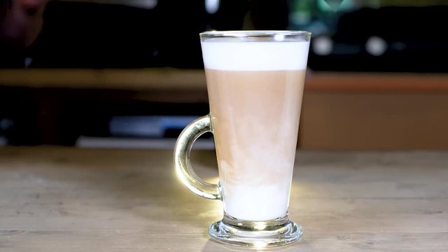 In the glass glowing mug with milk which stands on a wooden table, pour hot coffee