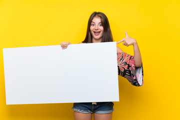 Caucasian girl in colorful dress over isolated yellow background holding an empty white placard for insert a concept