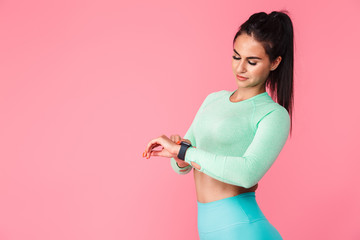 Pretty young sports fitness woman isolated over pink wall background using watch clock. - obrazy, fototapety, plakaty