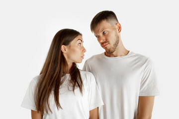 Beautiful young couple's portrait isolated on white studio background. Facial expression, human emotions, advertising concept. Man and woman standing, looking at each other seriously.