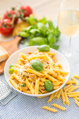 Pasta penne with chicken pieces mushrooms basil parmesan cheese and white wine.  Italian food in white plate on kitchen table