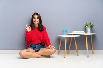 Young woman sitting on the floor showing an ok sign with fingers