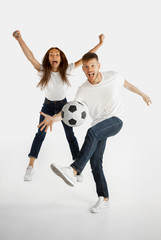 Beautiful young couple's portrait isolated on white studio background. Facial expression, human emotions, advertising, betting, sport concept. Man and woman playing football or soccer in action.