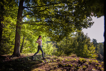 Young girl jogging in the woods on a sunny morning.