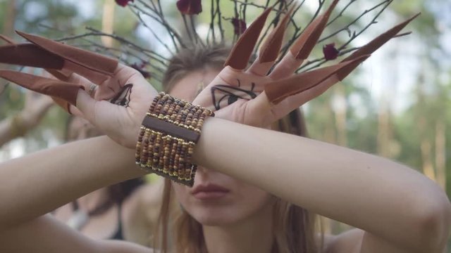 Hands of dryad or forest fairy with painted eyes on the palms and false claws dancing and covering face. Ancient ritual of forest creatures. Performance of dancers in forest