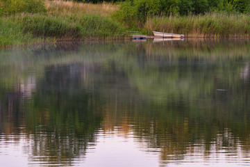 a small boat by a lake with forest reflecting in the water