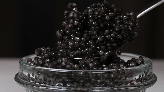 Black Caviar in spoon. High quality real natural sturgeon black caviar close-up. Delicatessen. Texture of expensive luxury caviar square dish on black. Seafood.