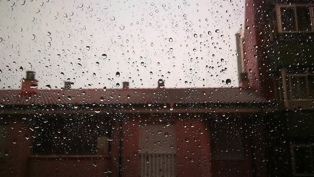 Lloviendo tras el cristal de la ventana con fondo de edificio y cielo blanco nublado