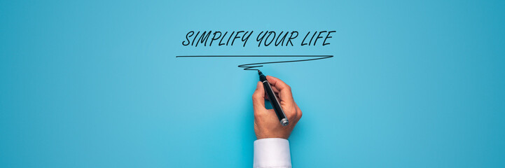 Male hand writing a Simplify your life sign with black marker over
