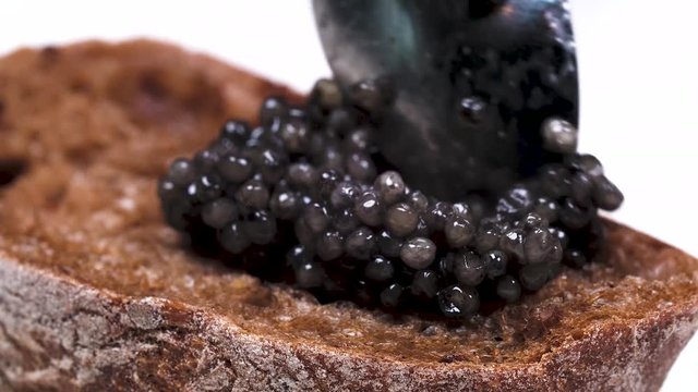 Spoon presses the hill of black caviar on a piece of white bread
