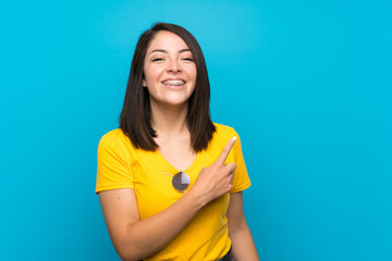 Young Mexican woman over isolated blue background pointing to the side to present a product