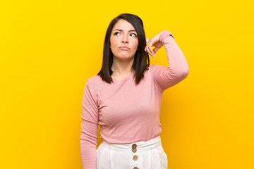 Young Mexican woman over isolated yellow background making the gesture of madness putting finger on...