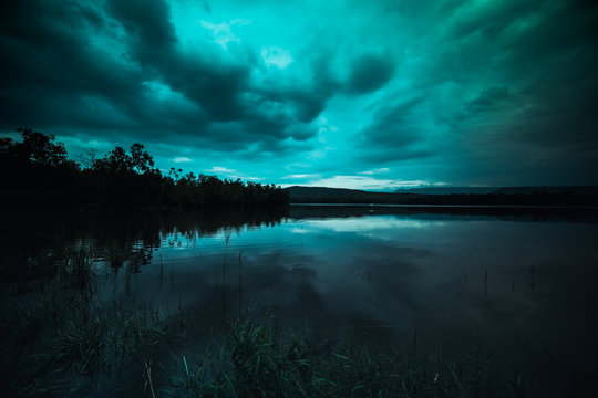 moonlight shines behind a cloudy at night over tranquil lake