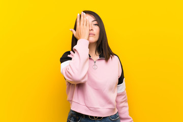 Young Mexican woman over isolated yellow background covering a eye by hand