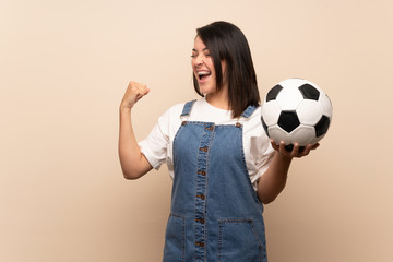 Young Mexican woman over isolated background holding a soccer ball