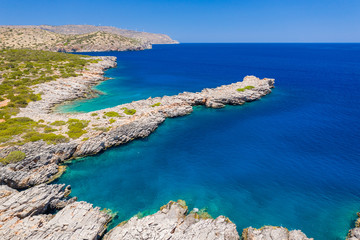 Aerial view of a clear, deep blue ocean and dry, yellow summer coastline (Kolokitha Island, Greece)