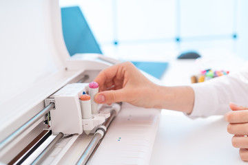 Young woman in printing office insert paper and color pens on plotter