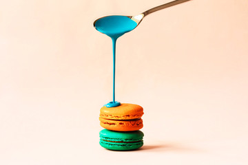 Liquid paint spills from a spoon on a macaroon on a pastel pink background. Copy space for text. Sweets in the modern version with the trend of receiving fluid liquids.