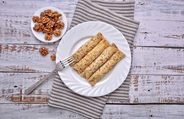 Pancakes and Walnut. Pancakes with filling on a white plate. Wood background. Rustic style. Rolled up pancakes ready for eating. Wrapped thin pancakes. Homemade thin crepes. Space for your text