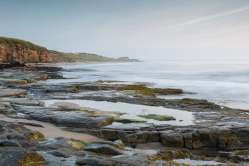 Sunrise and dawn light over the rocks on Cresswell Beach on the coast of Northumberland, England,...