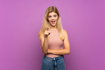 Teenager girl over isolated purple background surprised and pointing front