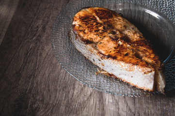 Close-up one grilled cum salmon keta fish steak on a glass transparent plate on a dark wood table background. A little overdone dish. Sea food for lovers of fried