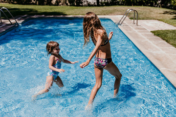 two beautiful sister kids at the pool playing, running and having fun outdoors. Summertime and lifestyle concept