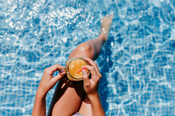 unrecognizable teenager girl at the pool drinking healthy orange juice and having fun outdoors. Summertime and lifestyle concept