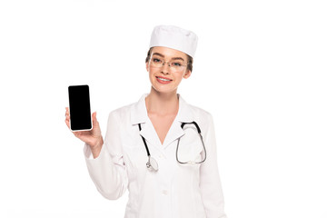 young happy doctor in white coat with stethoscope showing smartphone with blank screen isolated on white
