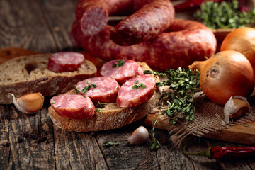 Dry-cured sausage with bread and spices on a old wooden table.