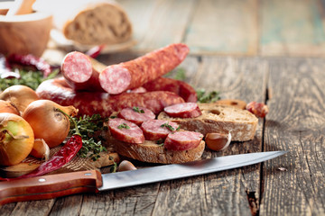Dry-cured sausage with bread and spices on a old wooden table.