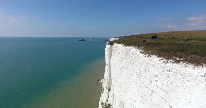 Flying along edge of white cliffs of Dover towards English Channel ferry crossing terminal, Kent, south east England on a sunny summer day .