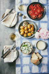 Fototapeta na wymiar Summer vegetarian dinner table for family or friends. Young baked potatoes, tomato carpaccio, cucumber salad, bread, wine, sauce and flowers over linen tablecloth. Flat lay, space