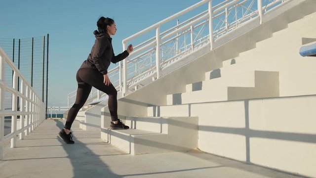 Sporty young woman makes cardio training running up on stairs slow motion