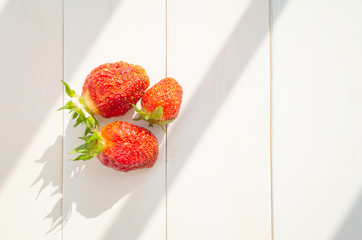 Ripe strawberries on a white wooden background. Bright sunshine. Concept of summer harvest of berries, healthy food. Minimalism, flat lay, top view. Place for text.