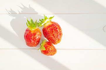Ripe strawberries on a white wooden background. Bright sunshine. Concept of summer harvest of berries, healthy food. Minimalism, flat lay, top view. Place for text.