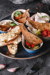 Healthy appetizer or snack with hummus, cod liver with ricotta, guacamole, rabbit sirloin, eggplant caviar in bowls over grey background. Healthy food, clean eating, dieting, top view