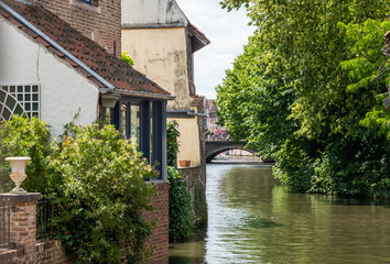 Fototapeta na wymiar Bruges, Flanders, Belgium - June 17, 2019: Green water canal with house and trees on side. Bridge in distance. Silver sky.