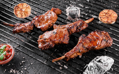 Grilled lamb ribs meat or rib eye with tomato sauce over the coals on a barbecue, dark background....