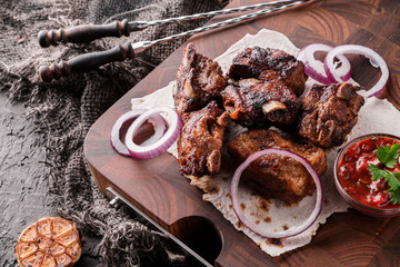 Grilled meat or shish kebab, shashlik with tomato sauce on wooden board over dark stone background. Top view