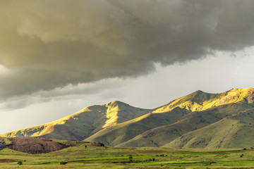 The Central Madagascar rural countryside with crop fields in the valley and rays of sunlight hitting the green mountains with rain clouds overhead  
