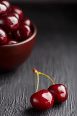 Ripe and juicy cherry berries on a black textural background in a brown cup, with water drops. Top view, close-up, Macro.
