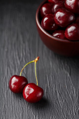 Ripe and juicy cherry berries on a black textural background in a brown cup, with water drops. Top view, close-up, Macro.