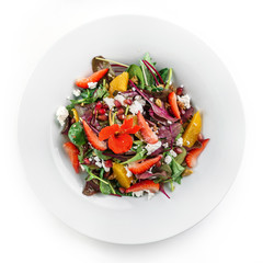 Healthy fresh salad with mix greens, strawberry, orange, nuts, cream cheese and edible flowers in plate on isolated white background. Healthy food, vegetarian dieting, top view