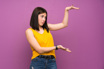 Young woman over isolated purple wall holding copyspace to insert an ad