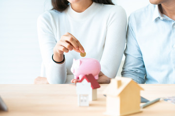 Obraz na płótnie Canvas woman putting a coin into a pink piggy bank concept for savings and finance.The best choice of house.House owner and architect discussing a choice.Couple dreaming of new home.
